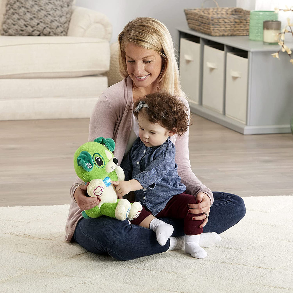 Green plush song-learning bear toy held by a child on the floor
