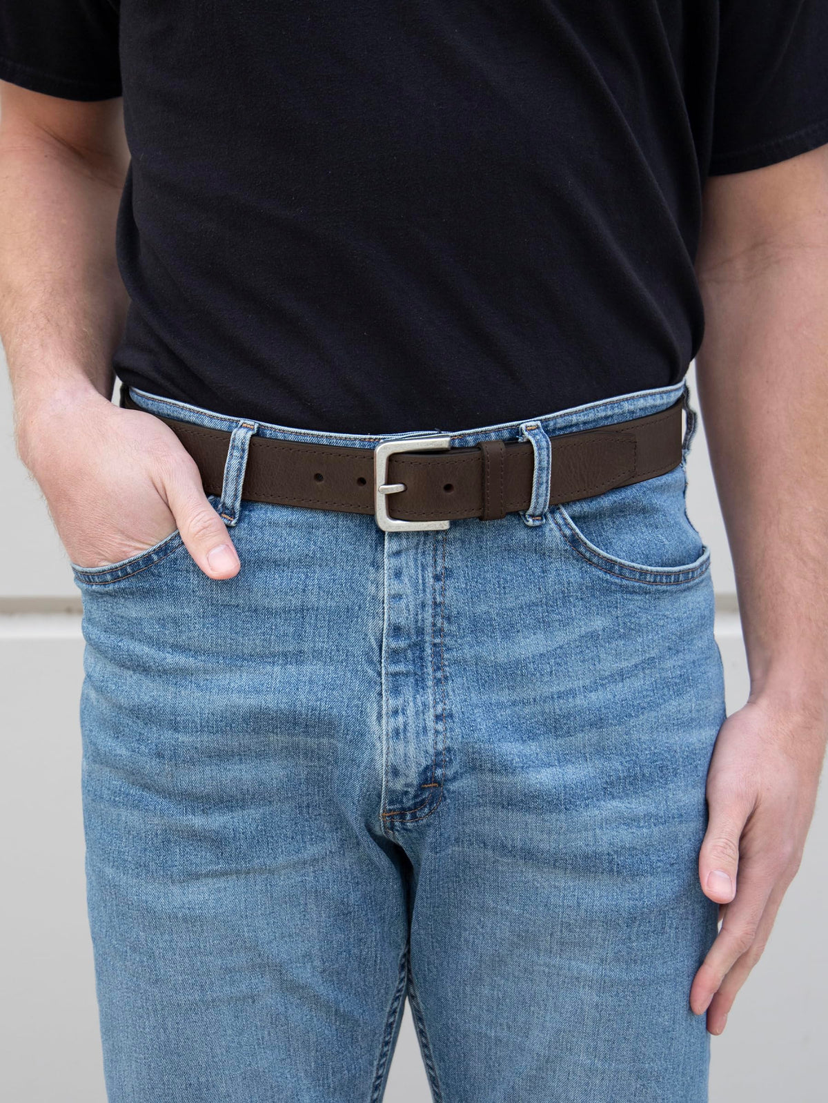 Brown leather belt with silver rectangular buckle on light-blue jeans