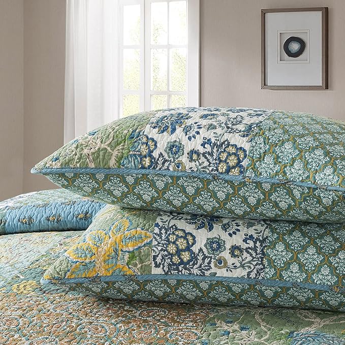 Stacked quilt and pillow layers in blue, green, and cream with decorative botanical print