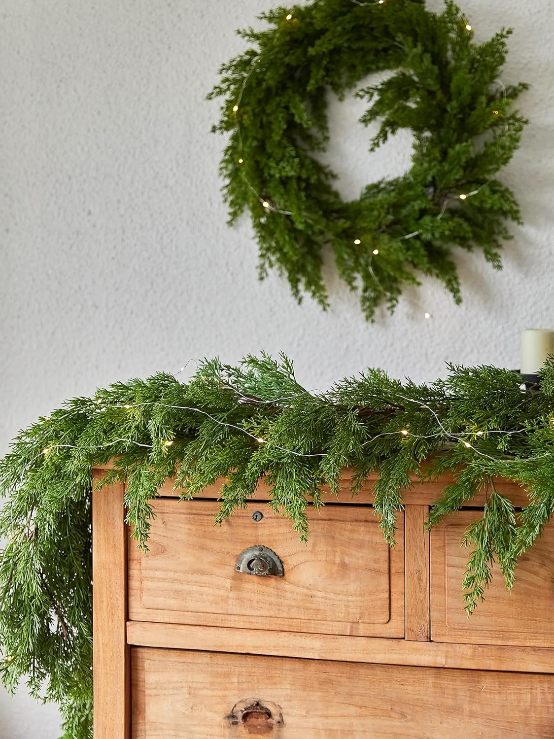 Artificial garland wreath-style loop with warm LED lights and pine needle texture, on wall