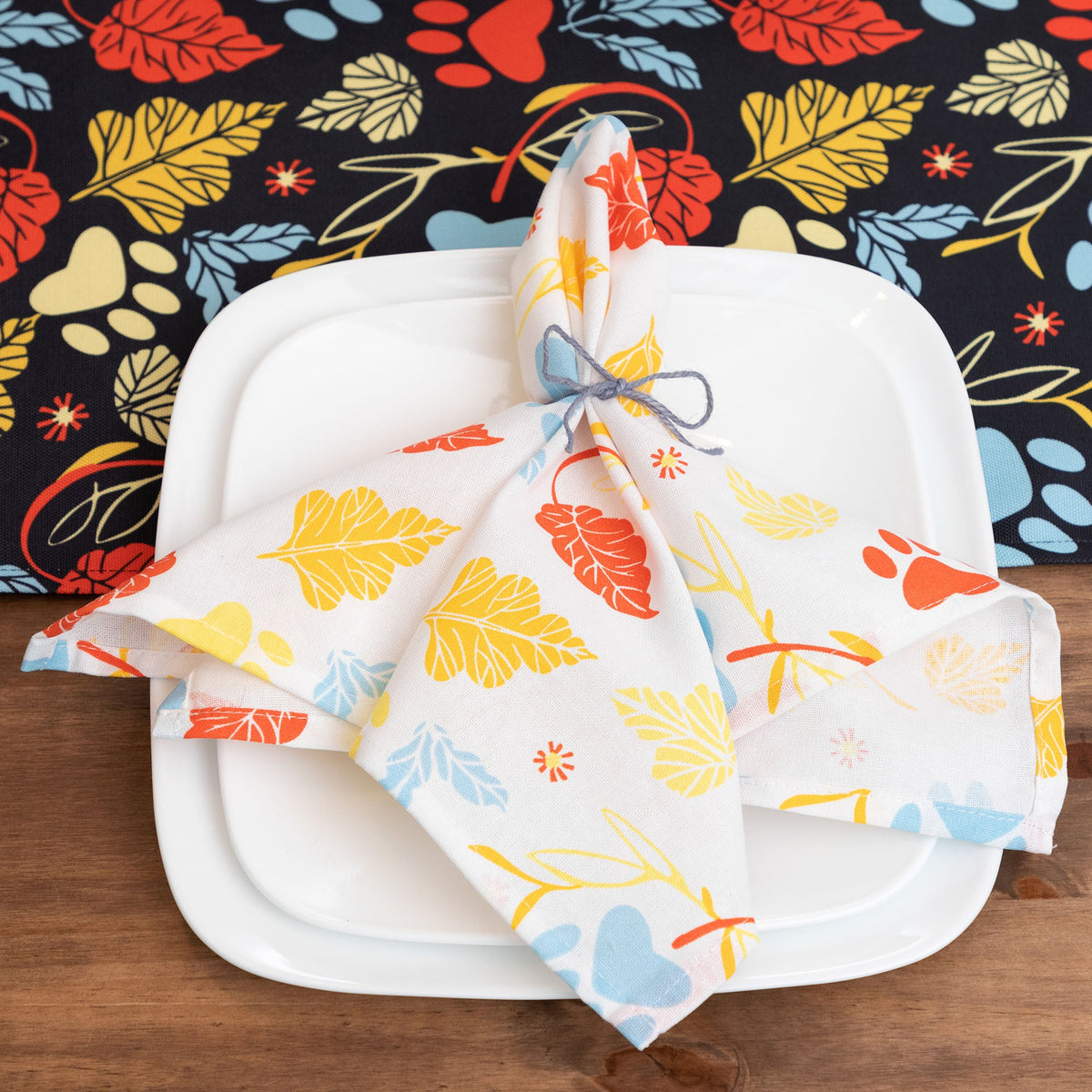 White table napkins set of 4 with colorful leaf and paw print, folded on plate