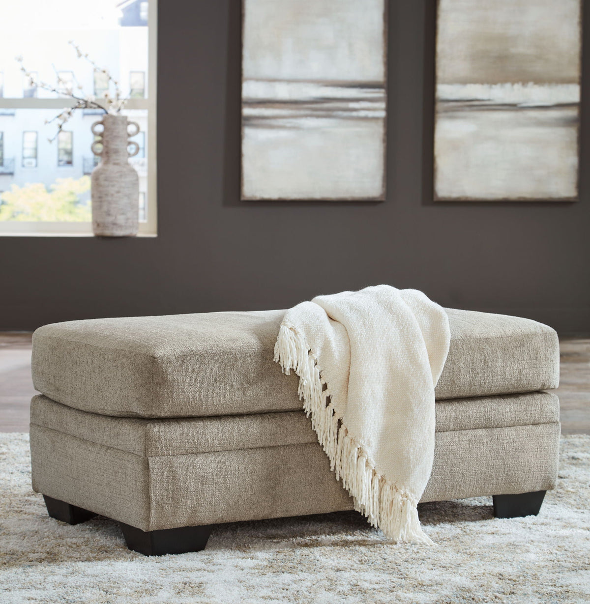Upholstered ottoman bench with square top and fringed throw, light beige fabric