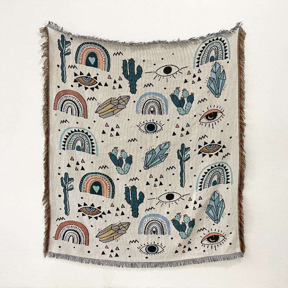 Evil eye patterned blanket in cream with cactus, rainbows, and eye motifs with fringe