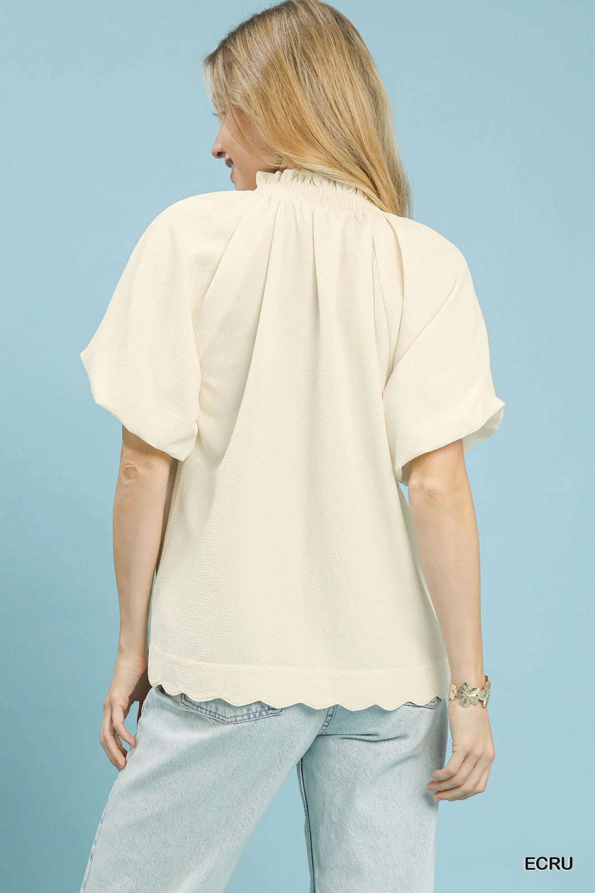 Back view of ecru textured blouse with pleated yoke, short puff sleeves, scalloped hem