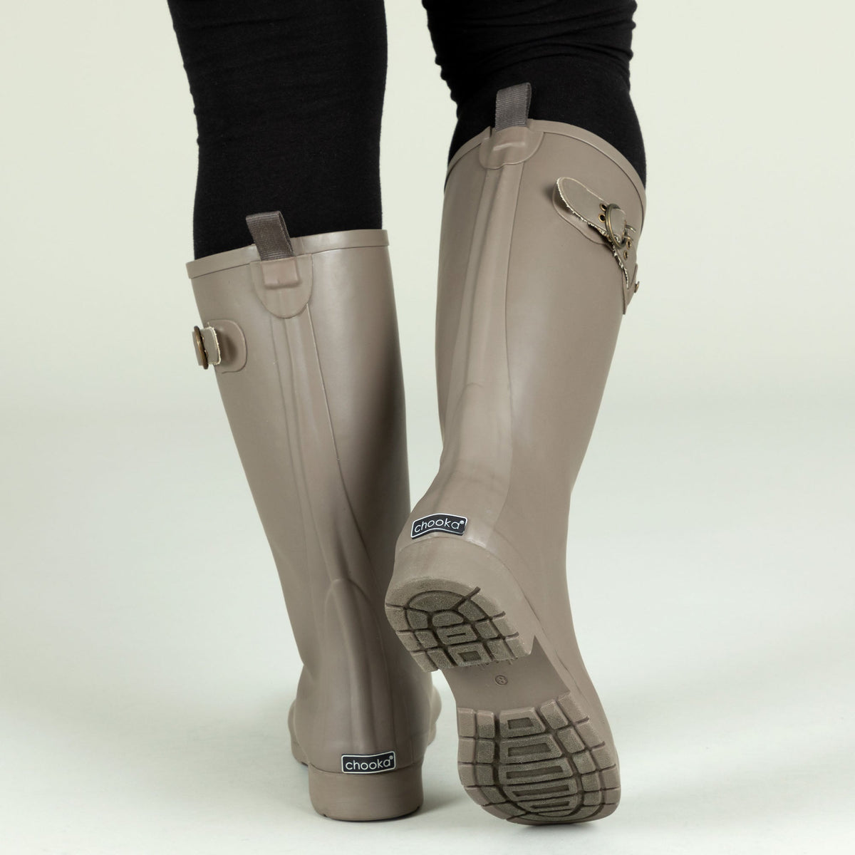 Taupe tall rain boots rear view with built-in logo patch and textured tread sole.