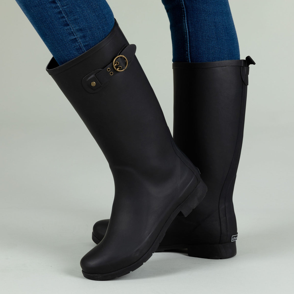 Black tall rain boots in side view with buckle strap and small heel logo patch.