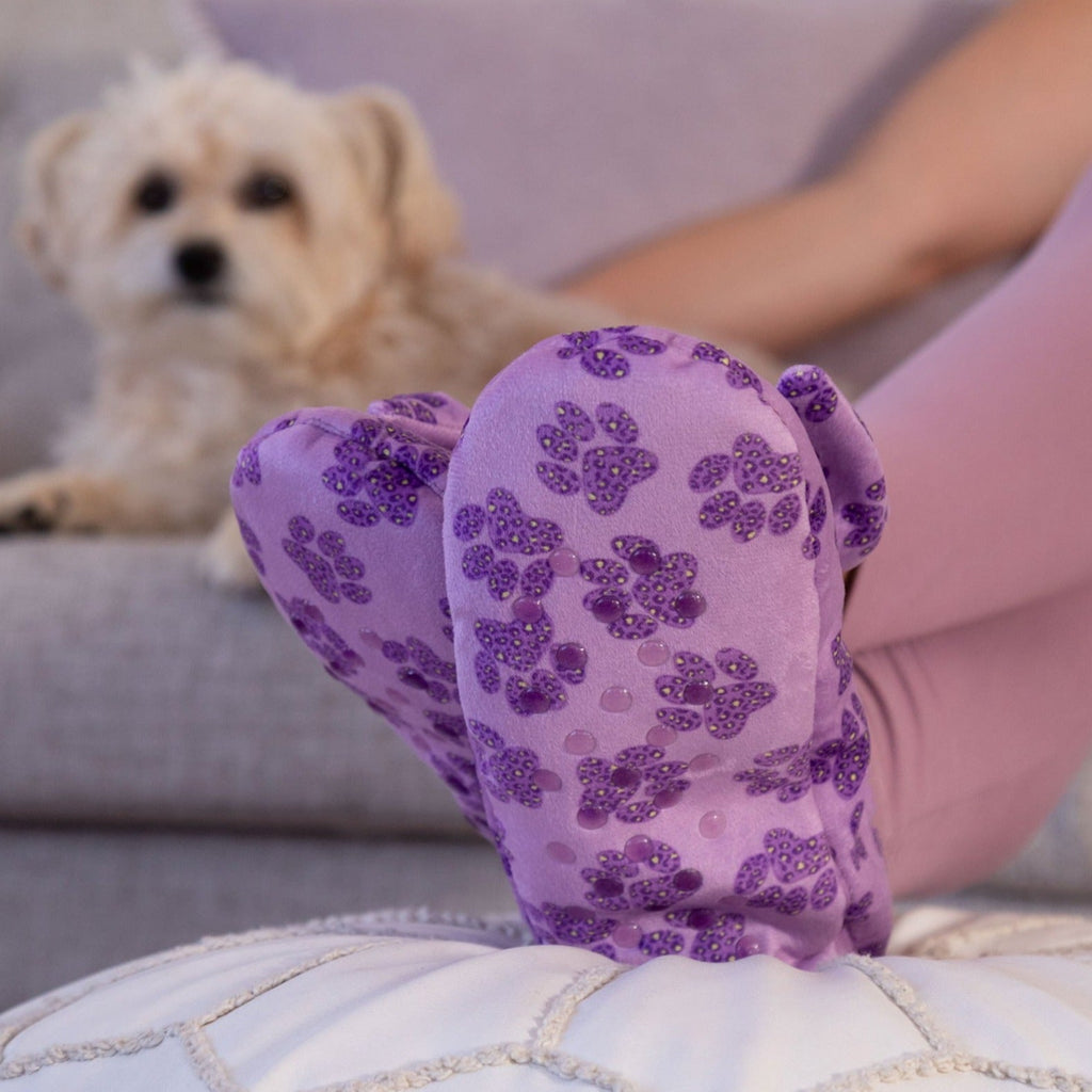 Purple leopard paw slippers with large bow and plush lining held up near a small dog