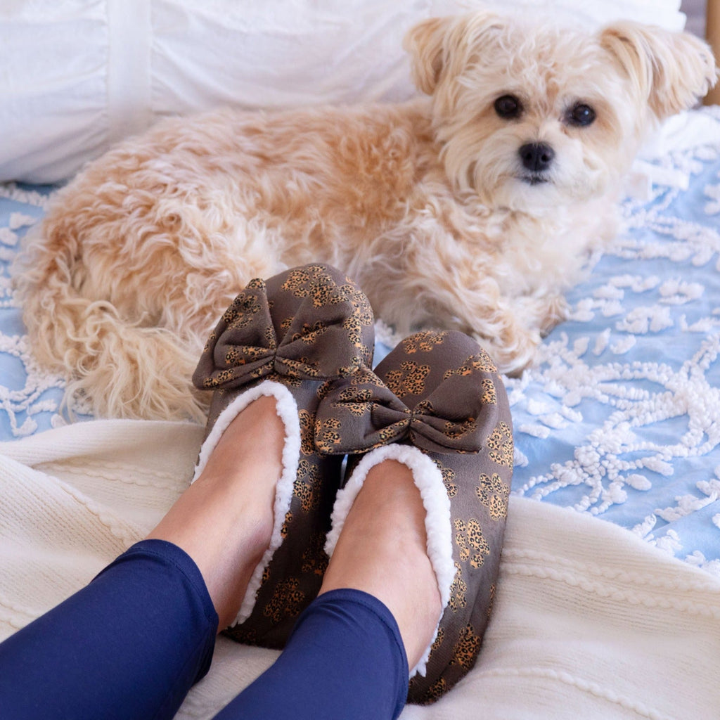 Brown leopard paw slippers with large bow and plush lining, shown on a bed