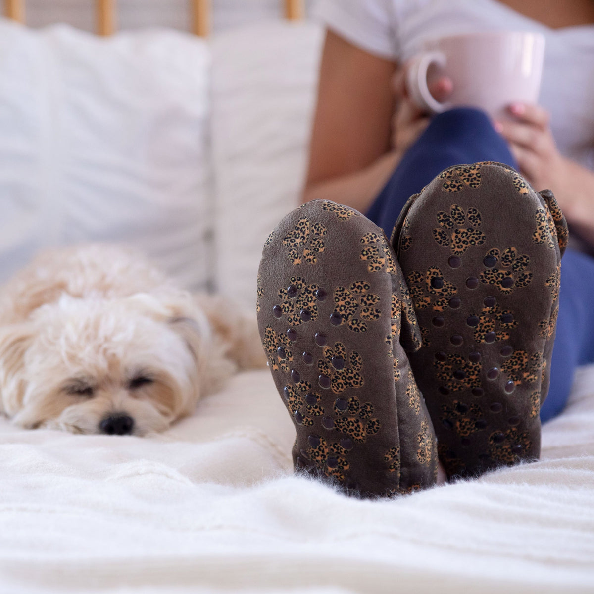 Brown leopard paw slippers with large bow, plush lining, worn indoors on a bed