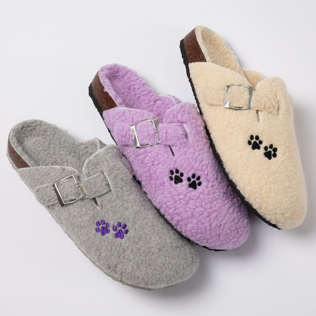 Plush sherpa clog slippers with paw print patches and buckle straps in cream, purple, and gray