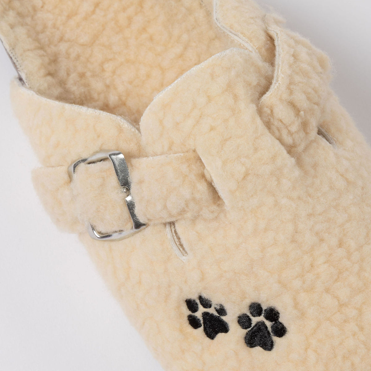 Cream sherpa slipper close-up with paw-print appliques and metal buckle