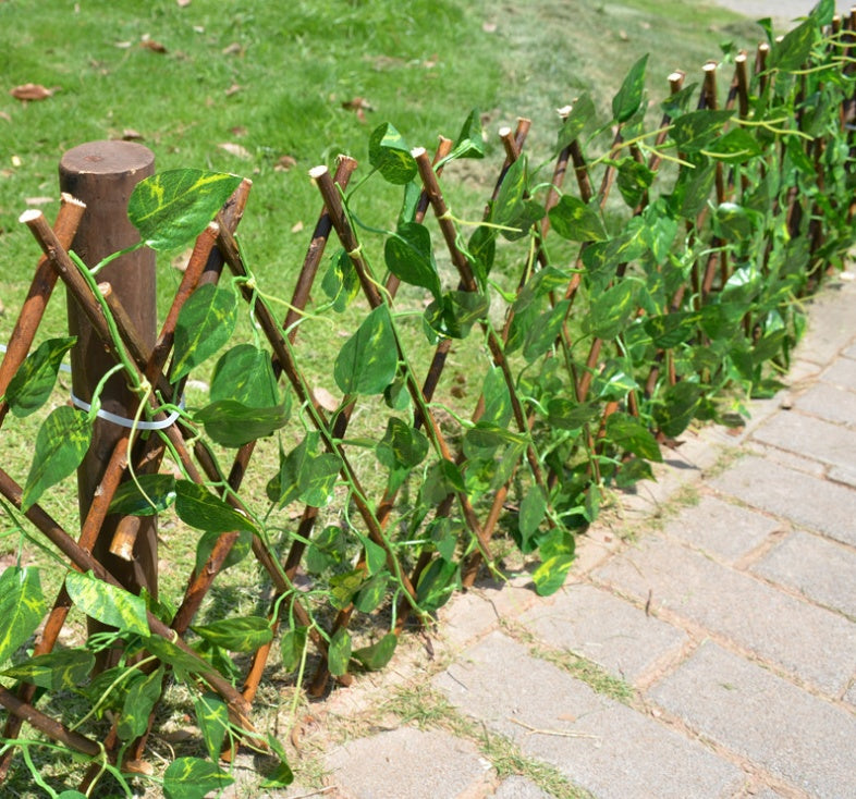 Expandable wooden plant trellis fence with green leaves along a walkway