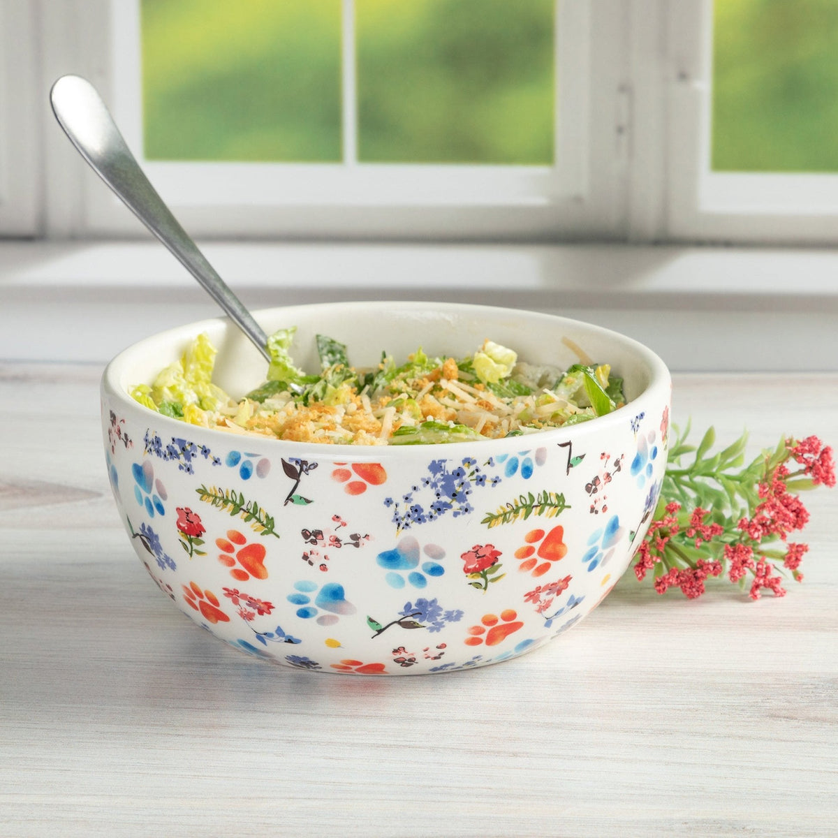 Ceramic soup bowl with colorful paw prints and floral pattern, filled with salad