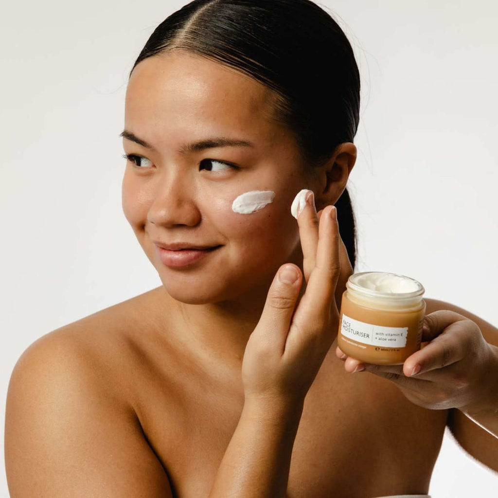 Woman applying face moisturizer cream to her cheek, holding an open jar