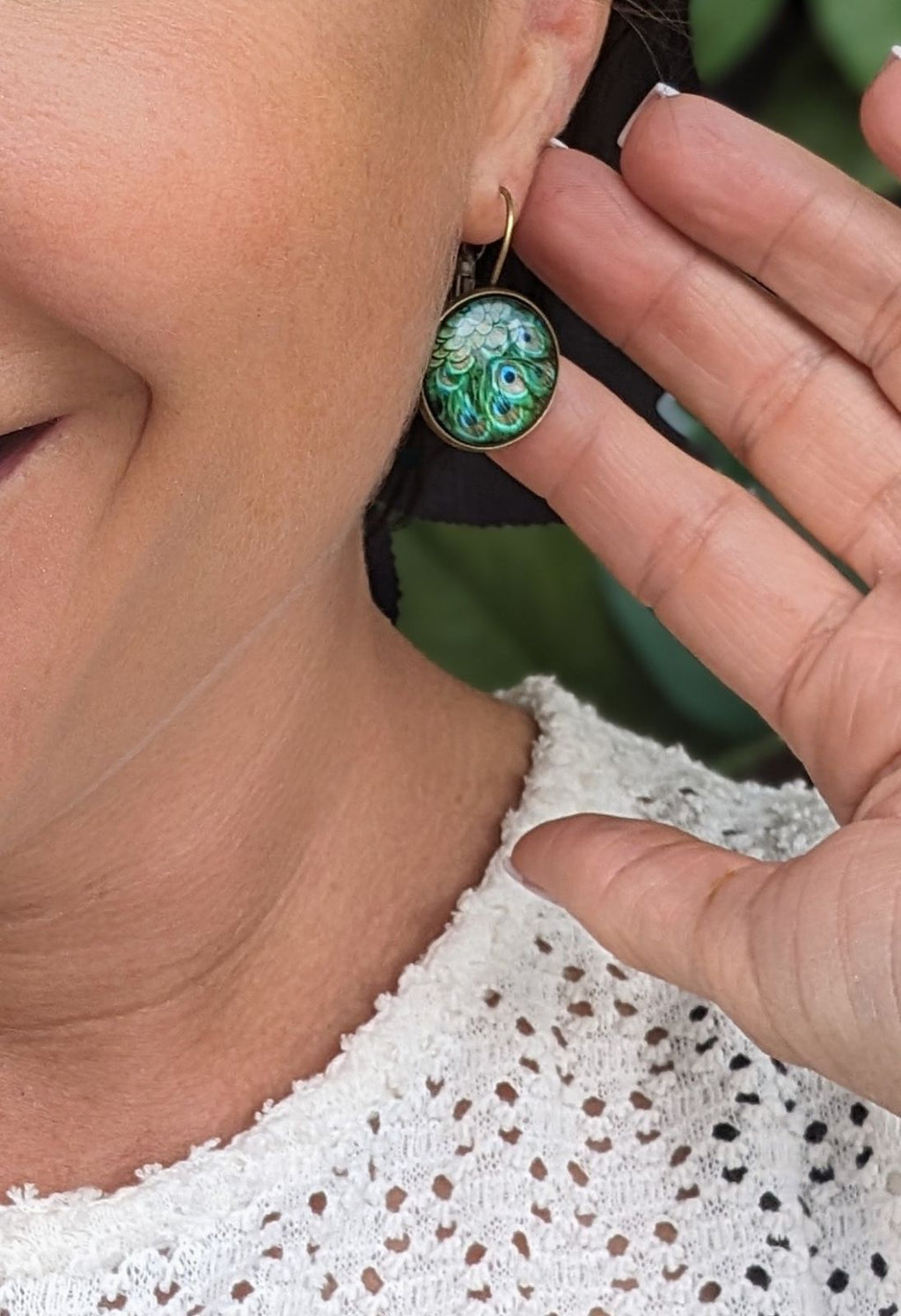 Teal green peacock-feather round earring on ear with bronze leverback hook