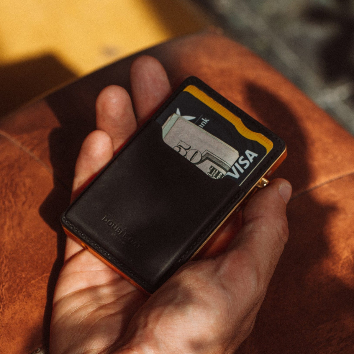 Black leather cardholder wallet with cards and yellow trim, held toward the camera.