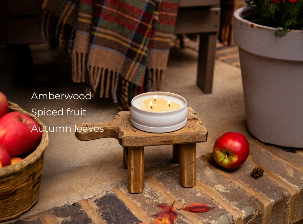Small lit 3-wick candle in a white round jar with autumn leaves around