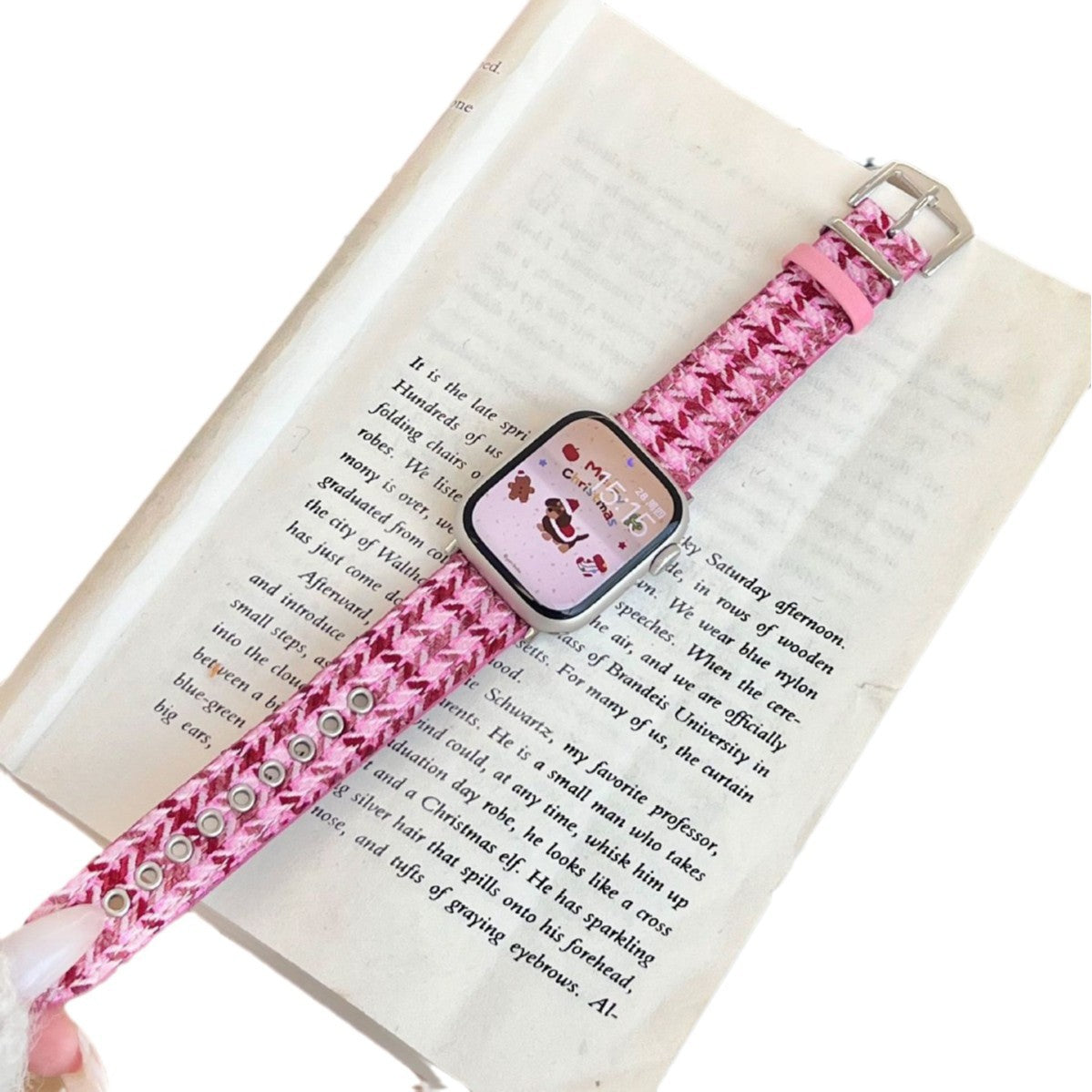 Christmas watch strap with bright pink woven fabric and metal clasp, shown on a book