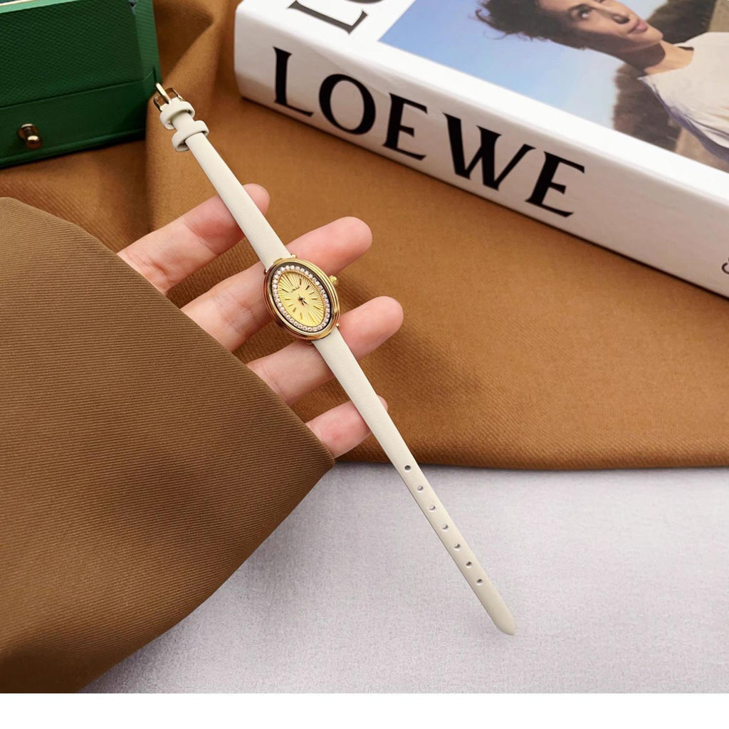Ladies gold watch with yellow dial and white strap, shown held in hand.