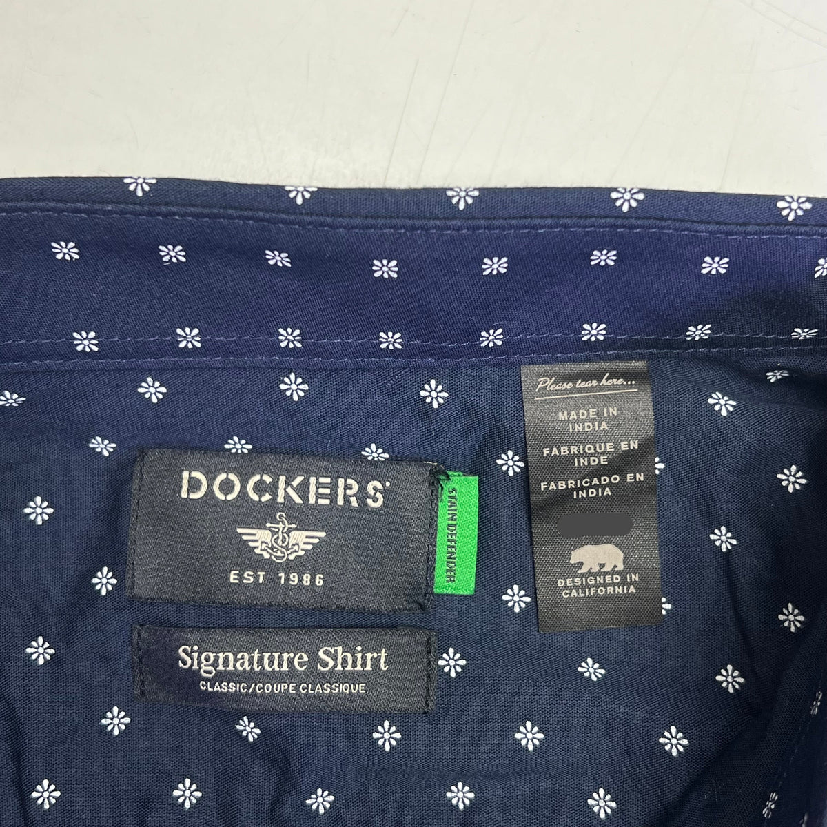Navy shirt with allover white daisy pattern and Dockers logo tag near hem.