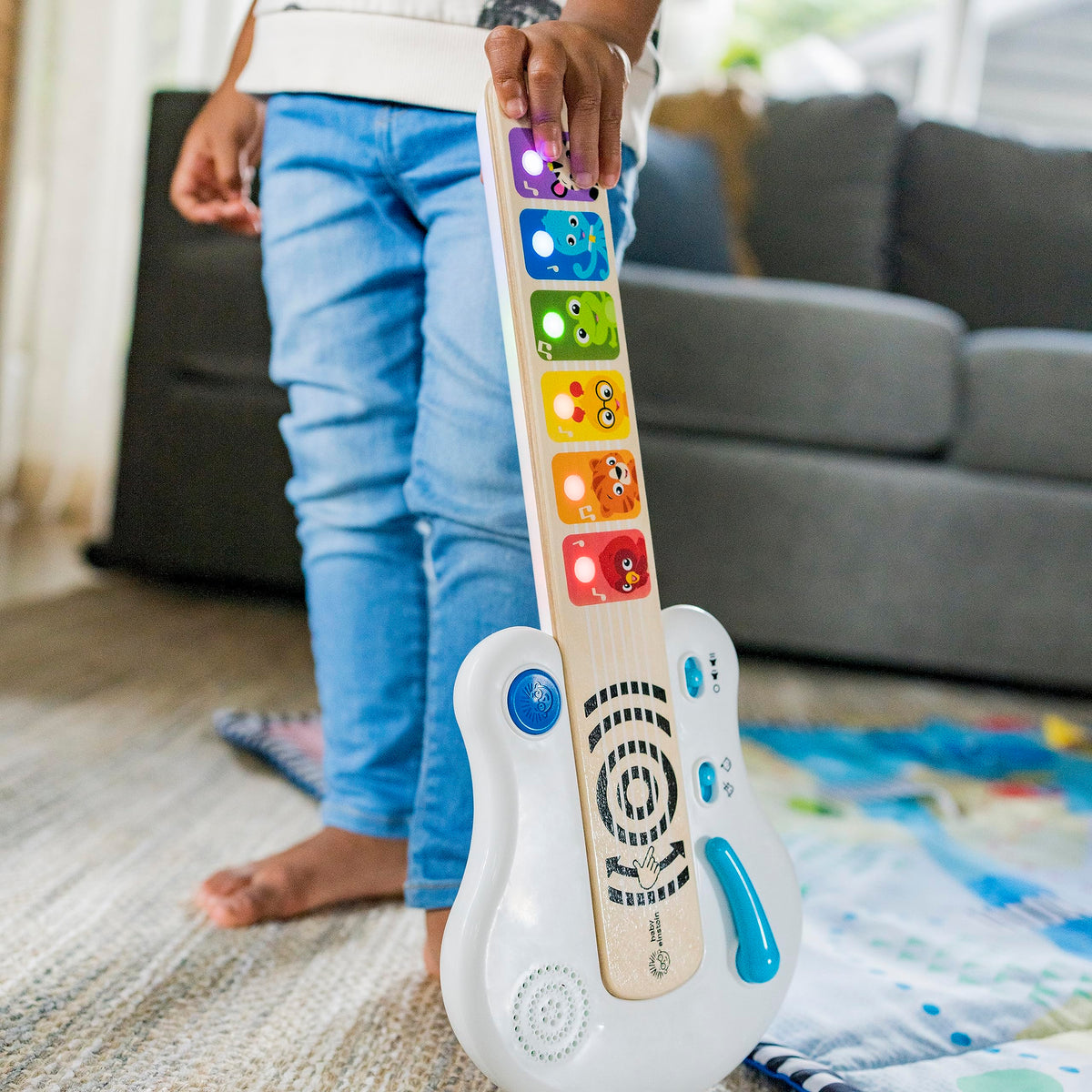 Light-up wooden guitar toy on the floor with colorful animal fretboard and blue side button