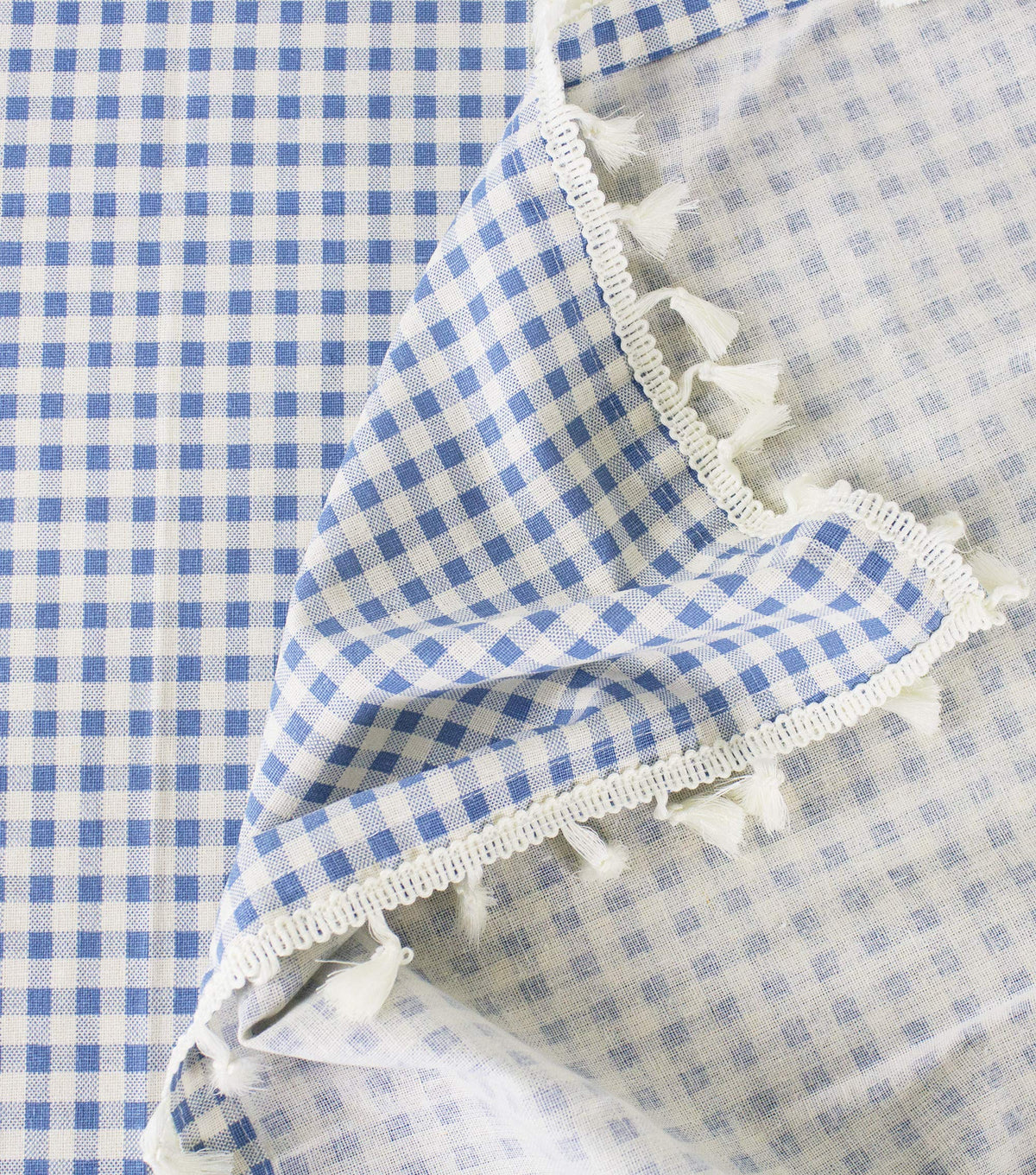 Blue and white gingham tablecloth corner with fringed trim and tassel details