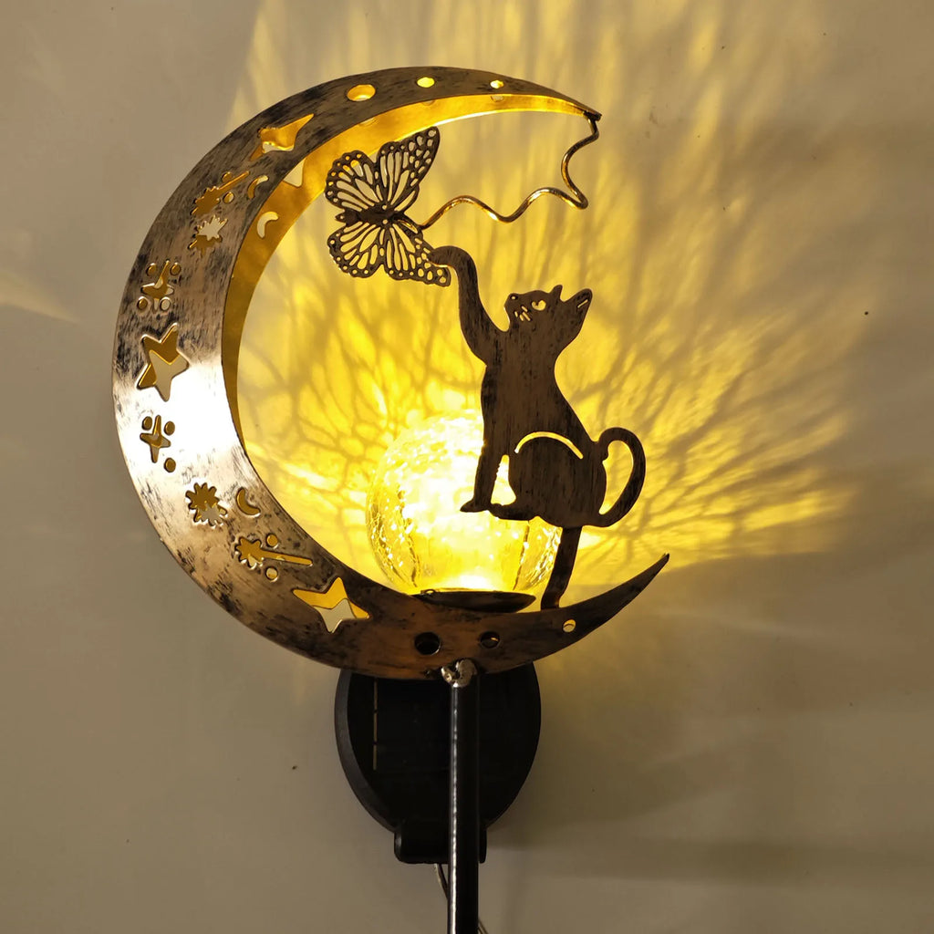 Close-up solar moon cat garden lamp with warm glowing bulb behind metal moon shade.