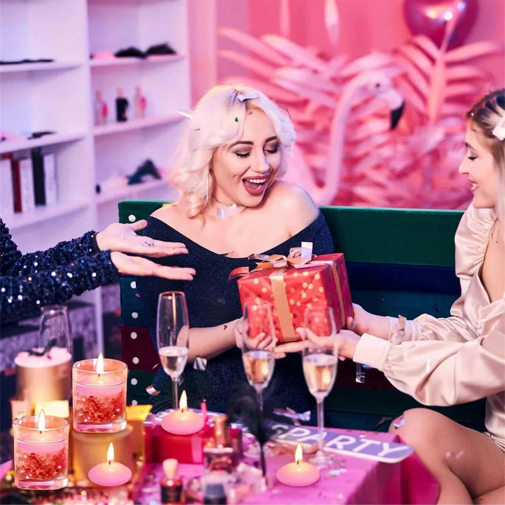 Pink floating candles with flames on party table beside wrapped gift and glasses