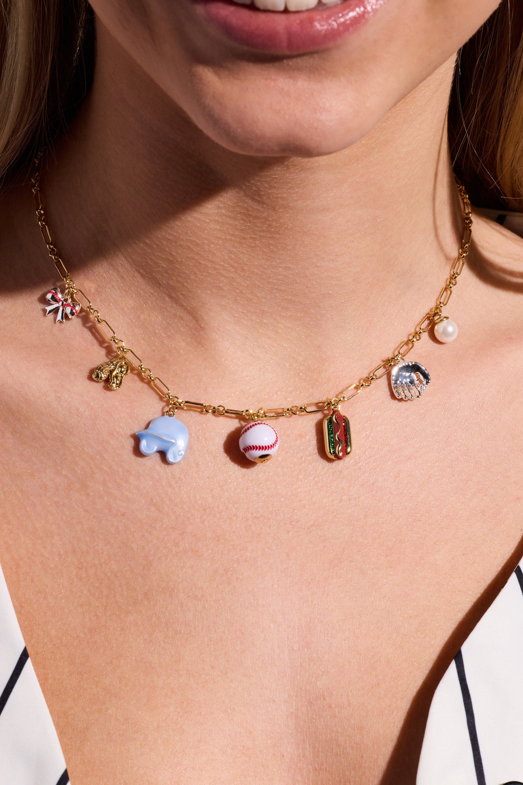 Gold-tone charm necklace on model with baseball, blue shoe, pearl, and red bottle charms