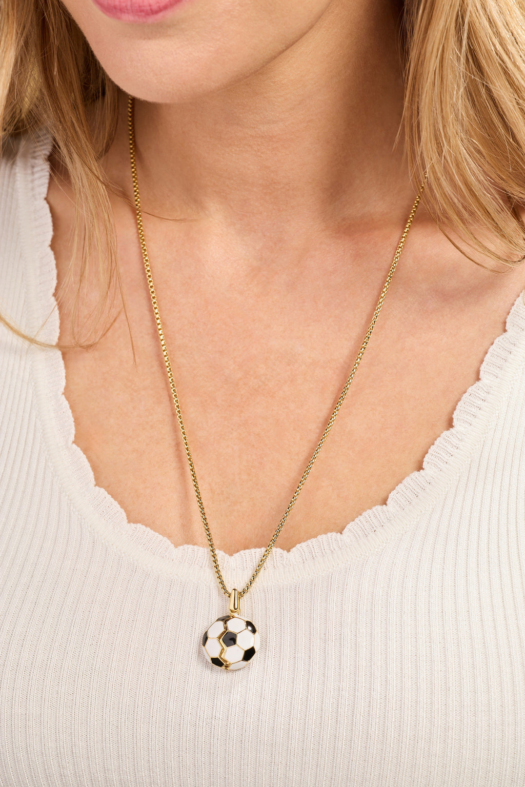 Gold soccer ball locket necklace worn on a cream ribbed top