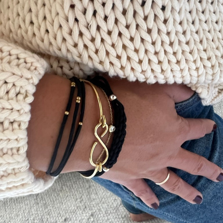 Braided hair tie bracelets on wrist, black cords with gold charms and rings