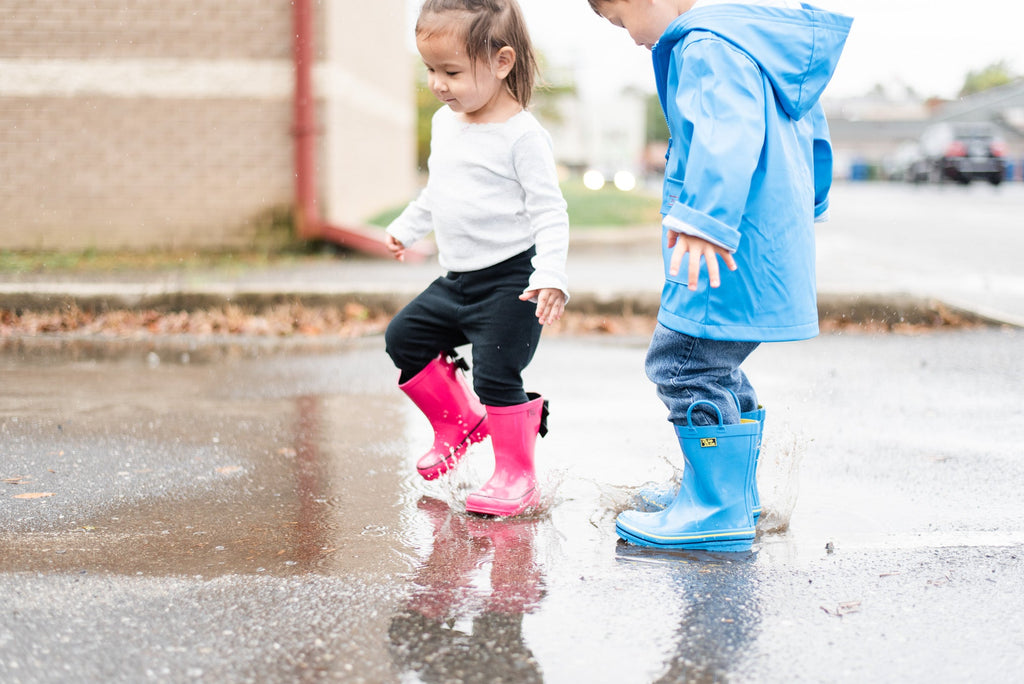 Kids' blue rain boots splashing in a puddle, yellow trim visible