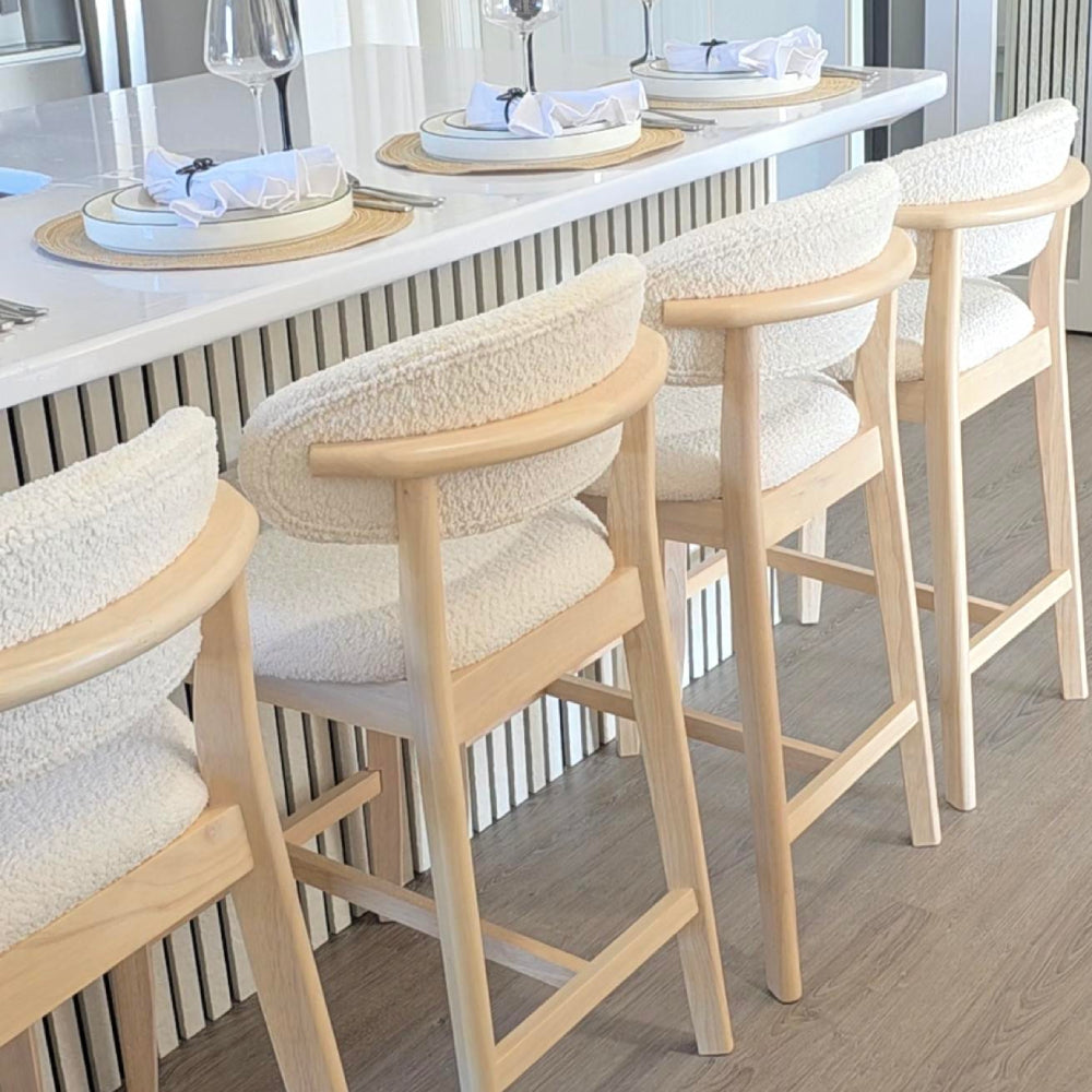 Cream upholstered bar stool with light wood legs and rounded back