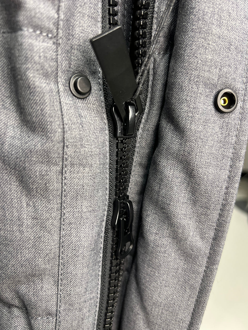 Grey coat front with black zipper and snap buttons near stand collar