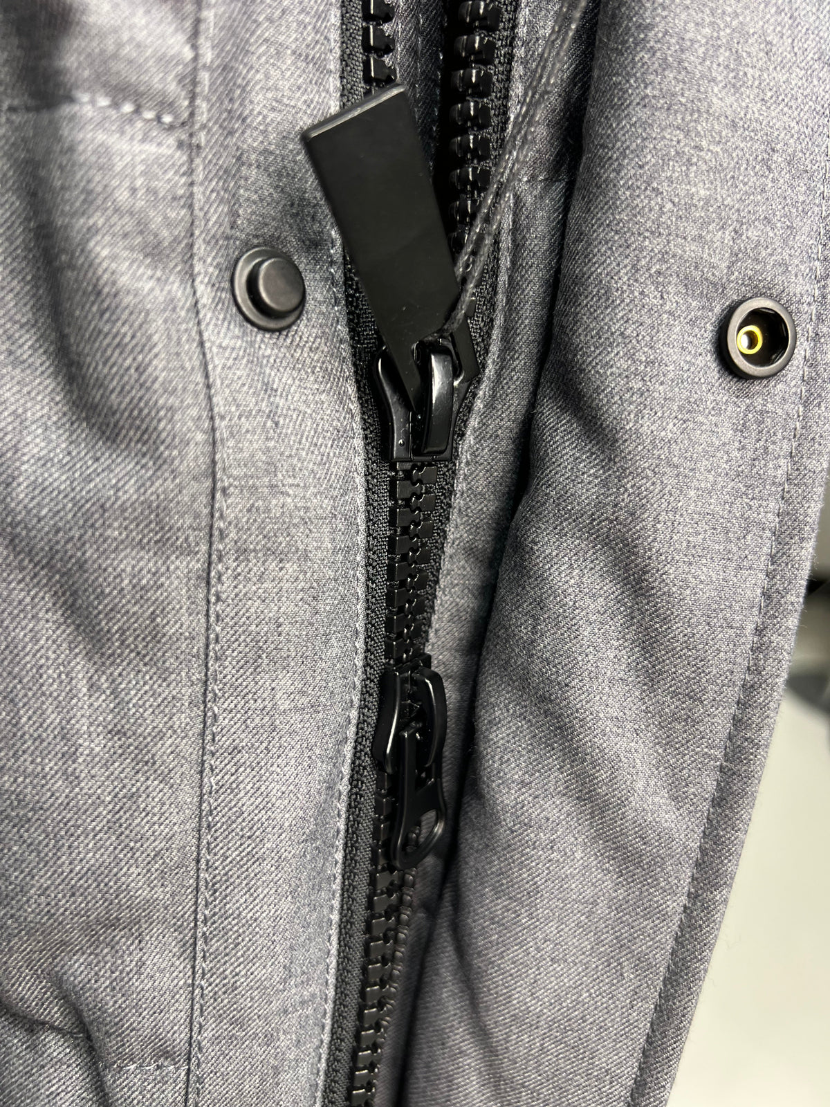 Grey coat front with black zipper and snap buttons near stand collar