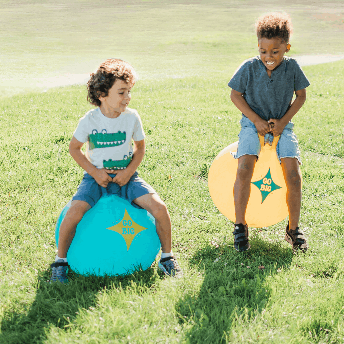 Two kids kneeling on teal and yellow handled hop balls for race play