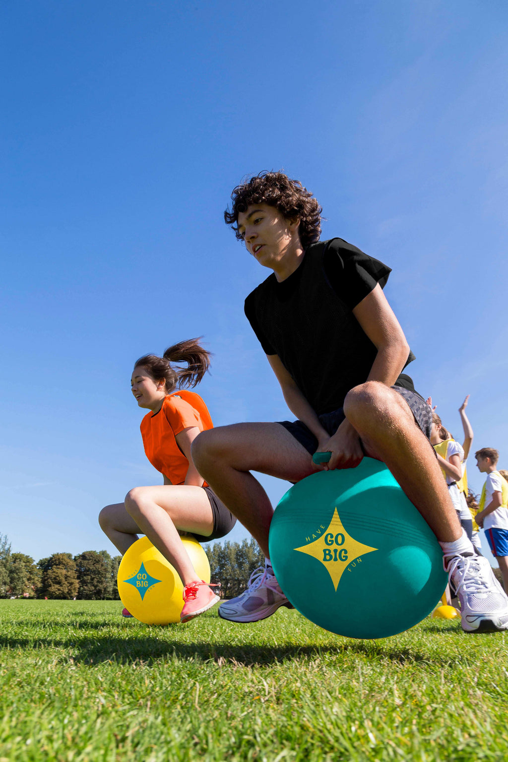 Kids sitting on teal and yellow handled hop balls with Go Big logo