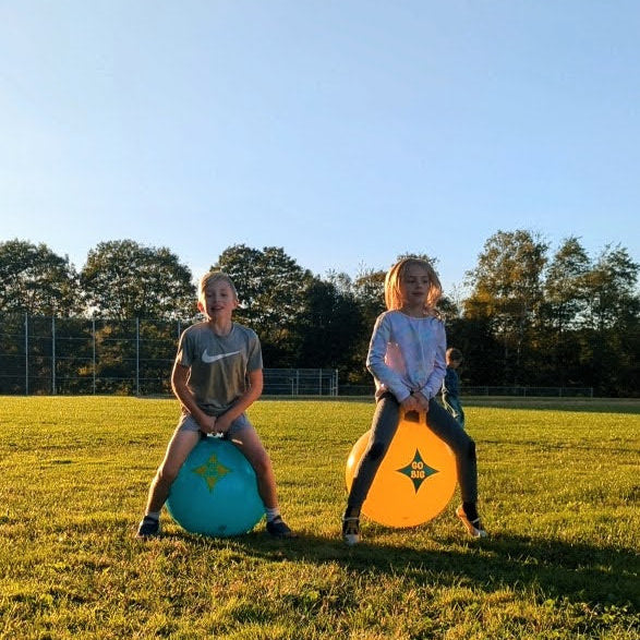 Two kids hopping on teal and orange handled hop balls with Go Big logos