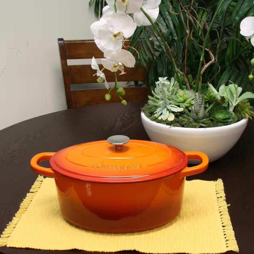 Orange enameled Dutch oven with lid and side handles on table