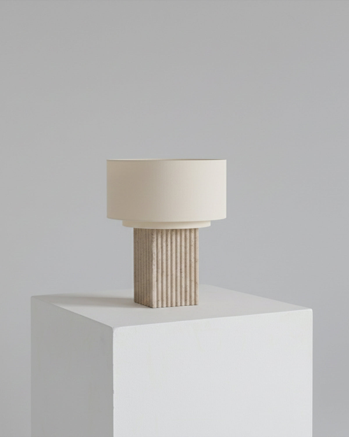 Table lamp on plinth with off-white shade and ribbed tan base