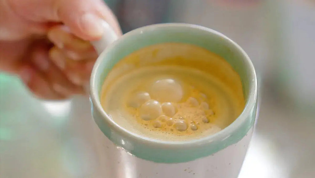 Glass mug filled with creamy yellow turmeric drink with bubbles