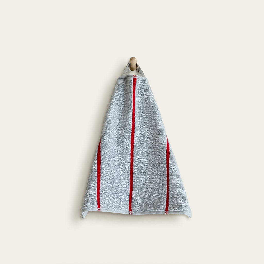 Cotton kitchen towel in light blue with bold red vertical stripes, hanging