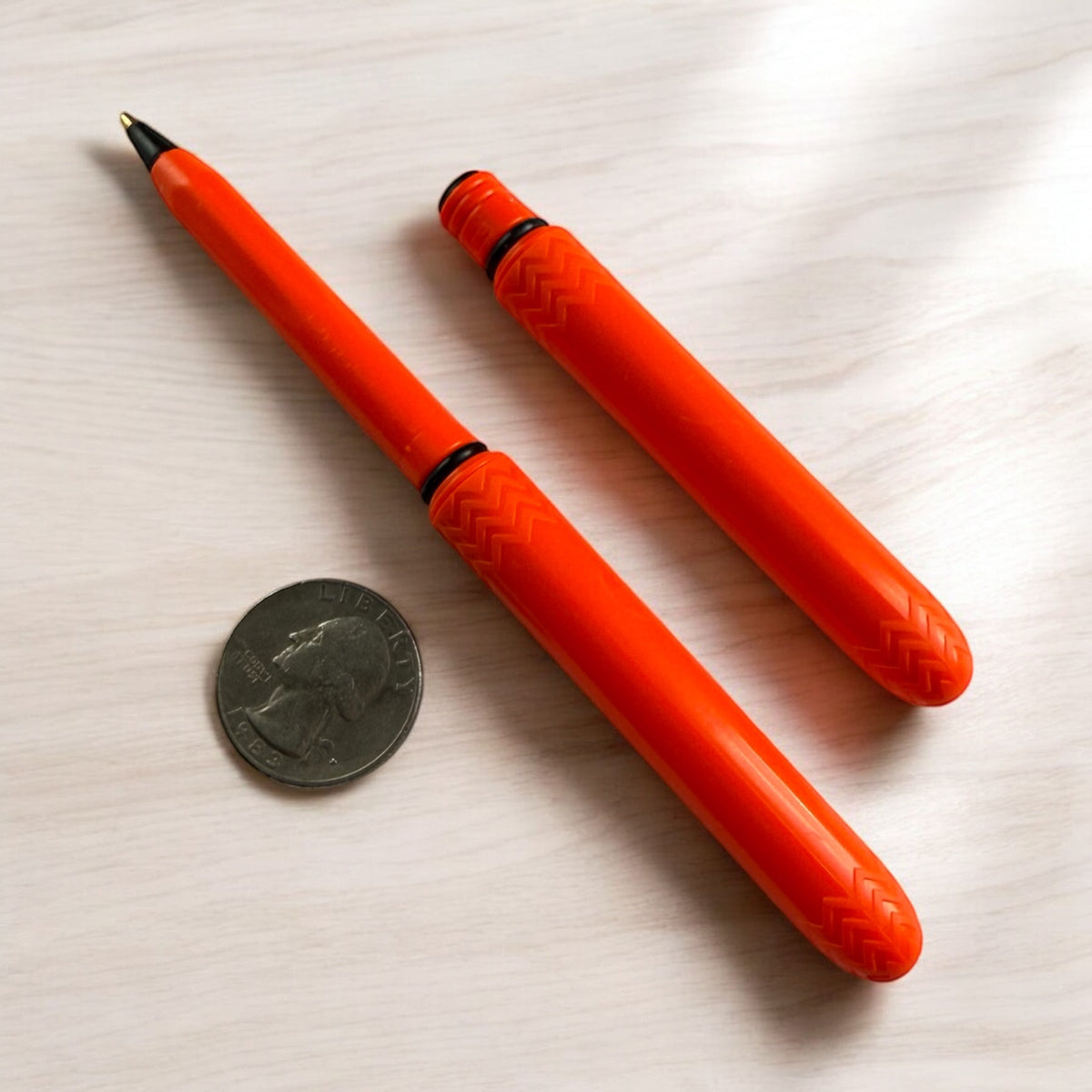 Blaze orange pocket pen pack with coin for scale, two pens with black tips