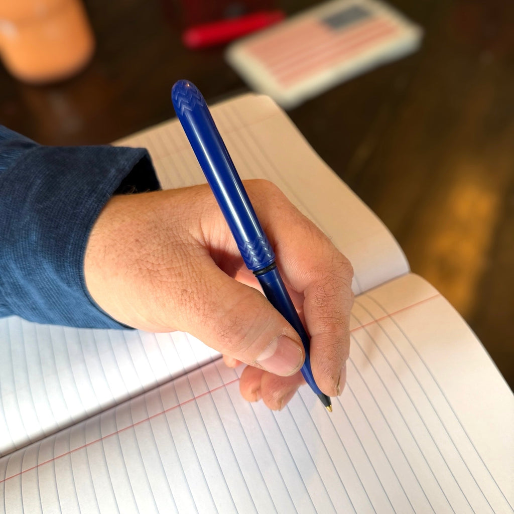 Blue indigo pocket pen in hand writing on lined paper, textured grip
