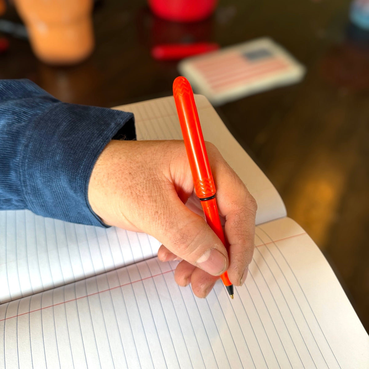 Blaze orange pocket pen in hand writing on lined paper, textured grip