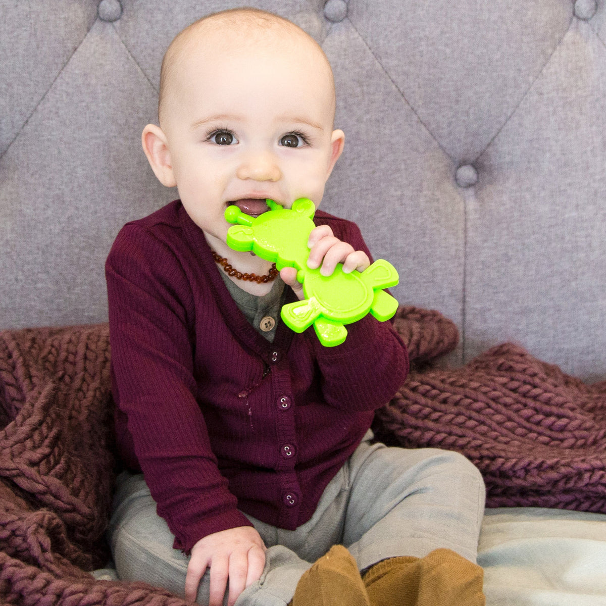 Baby holding lime green giraffe teether with textured chew areas