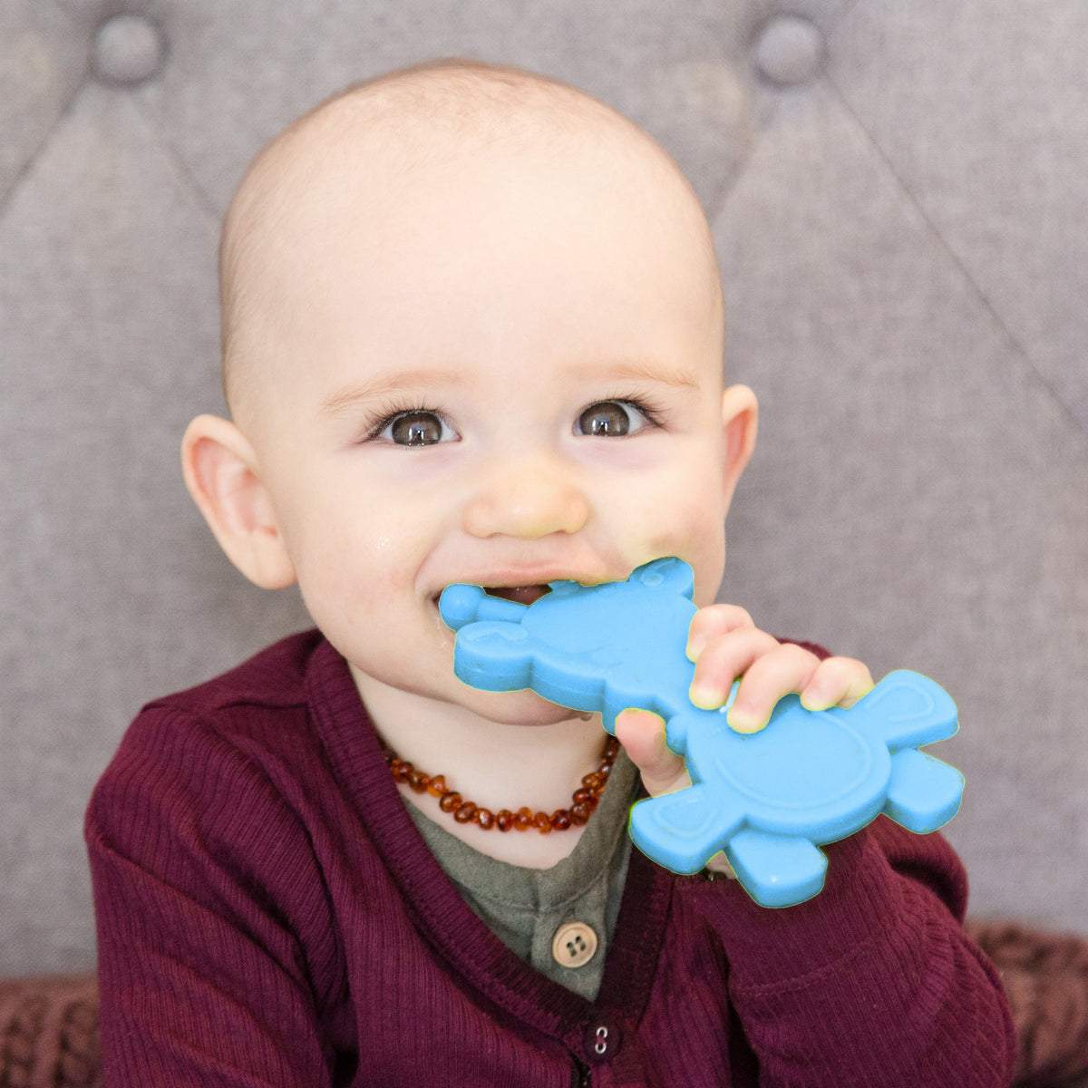 Baby holding a cyan giraffe teething toy with textured chewing surface