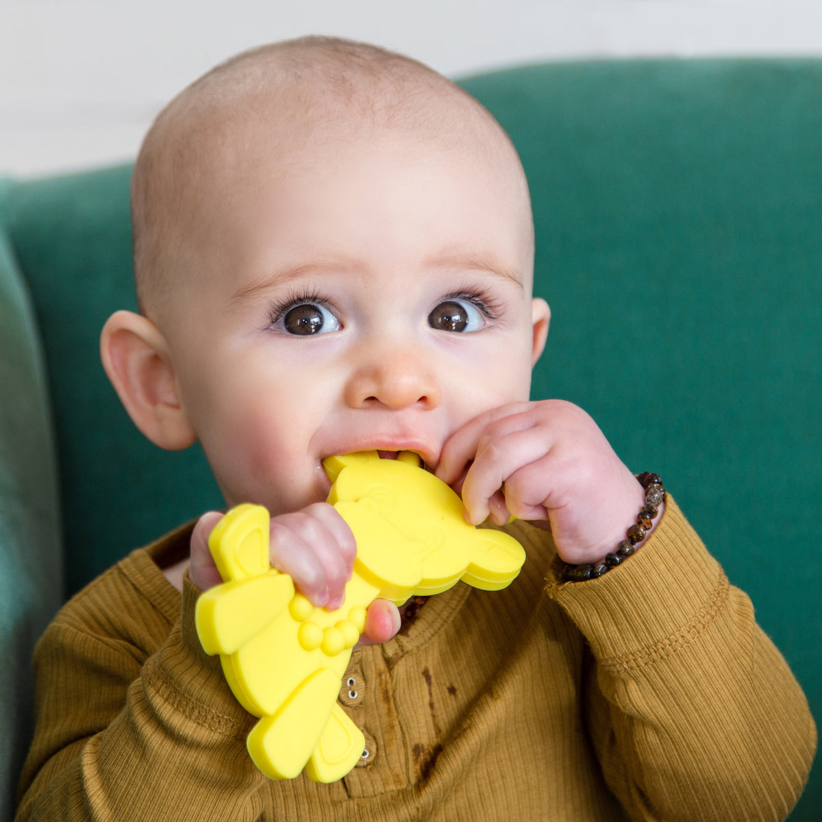 Baby holding a yellow giraffe teething toy with textured, flexible nubs