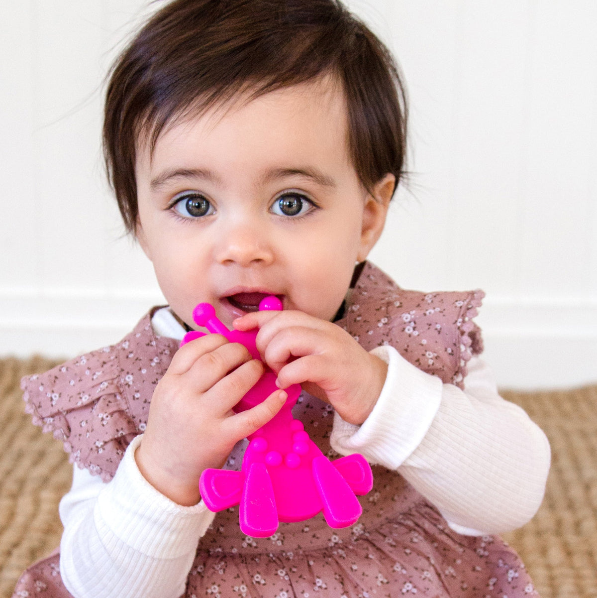 Magenta baby teething toy in toddler hands, being chewed at the bumpy end