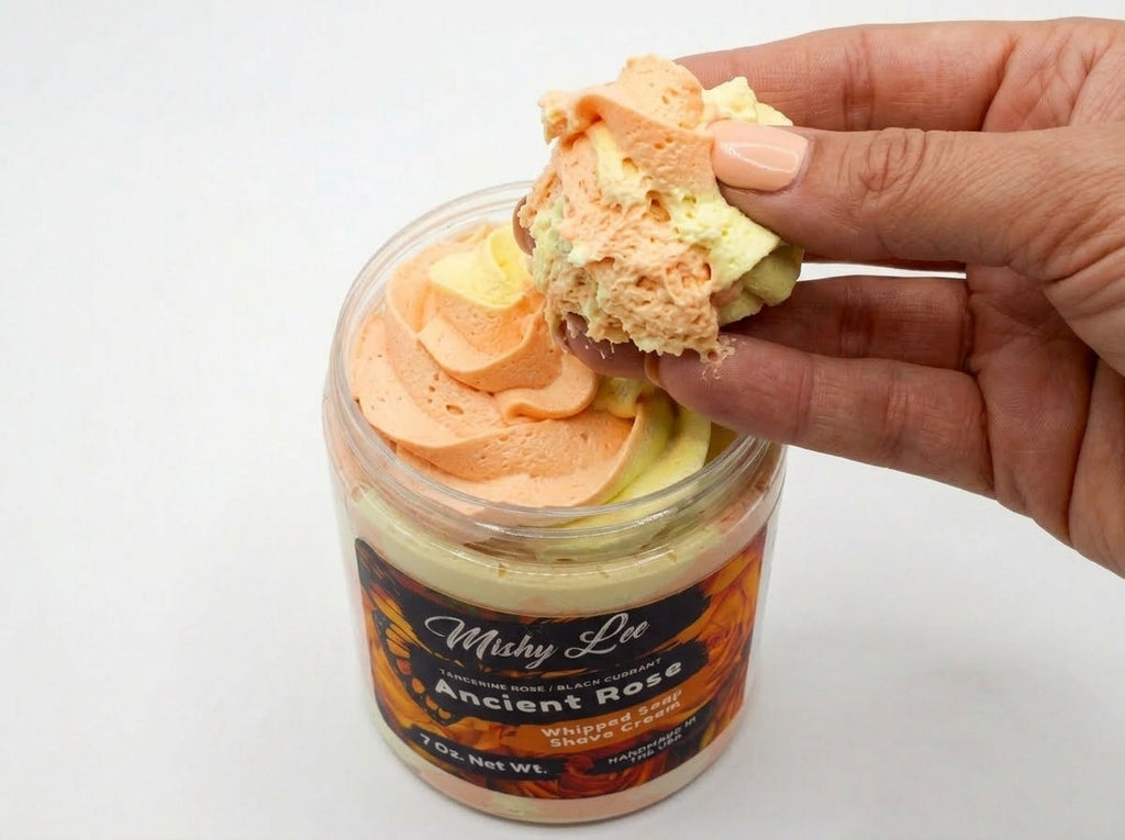 Hand holding scoop of orange-yellow whipped soap and shave cream above jar